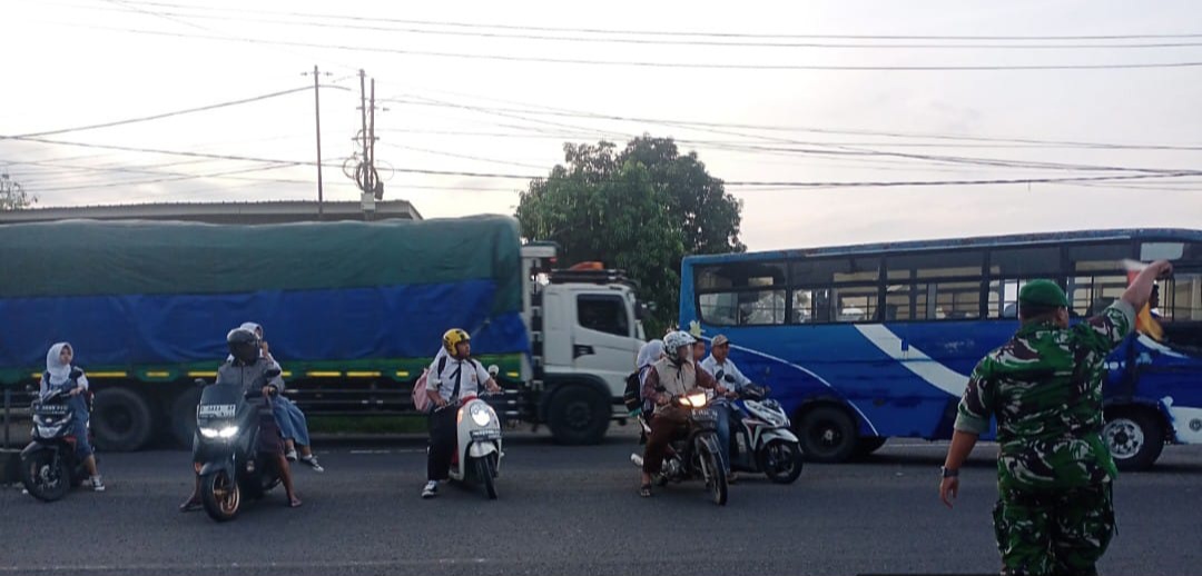 Anggota Koramil 1605 Sukagumiwang Indramayu Bantu Menyeberangkan anak sekolah di Jalan Raya Candangpinggan