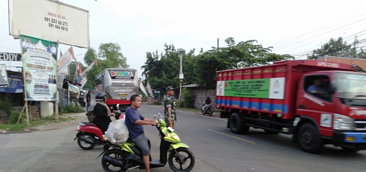 Babinsa Koramil 1609 Juntinyuat Bantu Masyarakat dan Anak Sekolah Menyeberang Jalan Raya Desa Juntikebon 